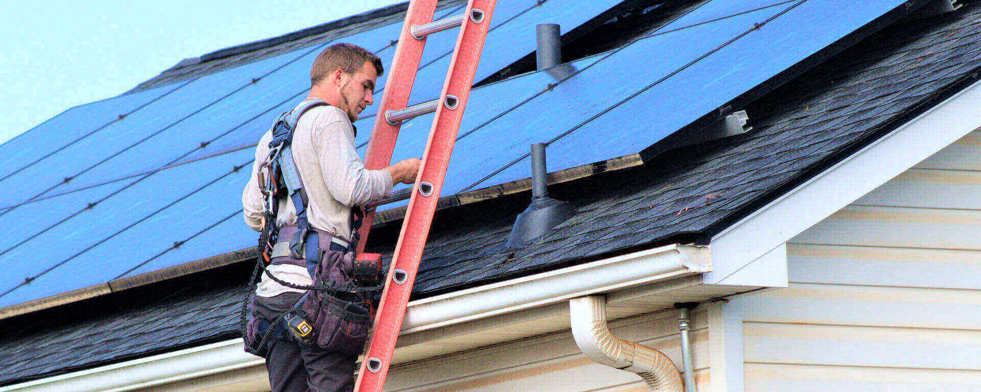 Technician on a ladder accessing rooftop solar panels